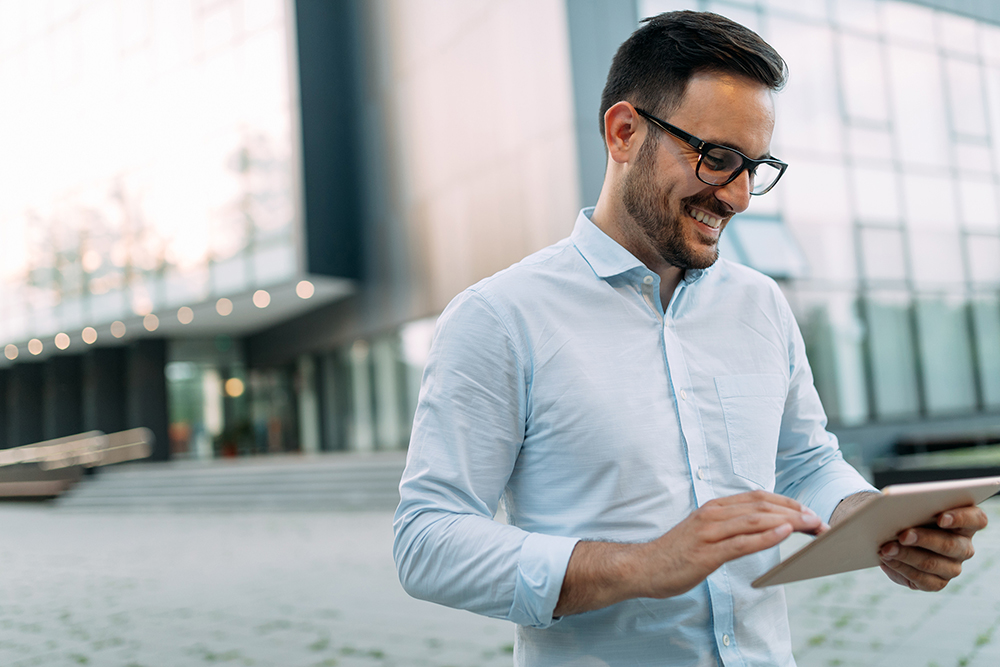 Happy businessman using tablet outside office building.