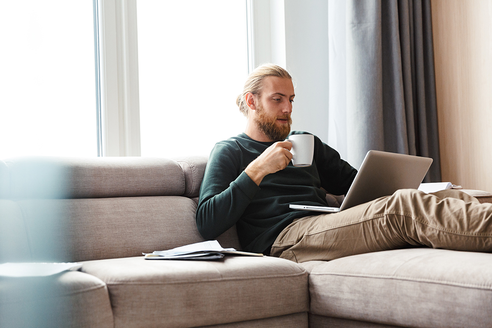 Man on lounge working with laptop having coffee.