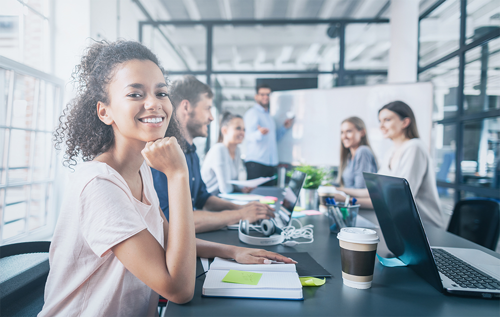 Happy young woman with colleages in office staff room looking at camera.
