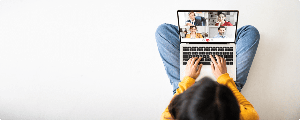 View from above. Young woman cross legged sitting on floor with laptop in lap meeting with four people on a video call.