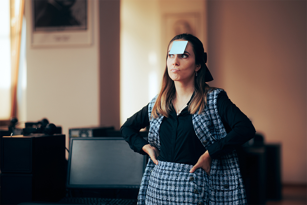 Business woman with sticky note on forehead hands on hips.
