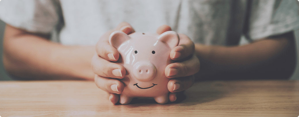 Hands holding pink piggy bank on wood table