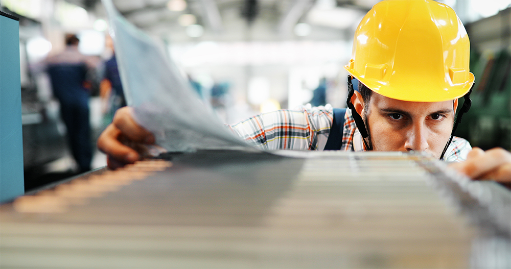 Workman in factory checking specs on machinery with paperwork.