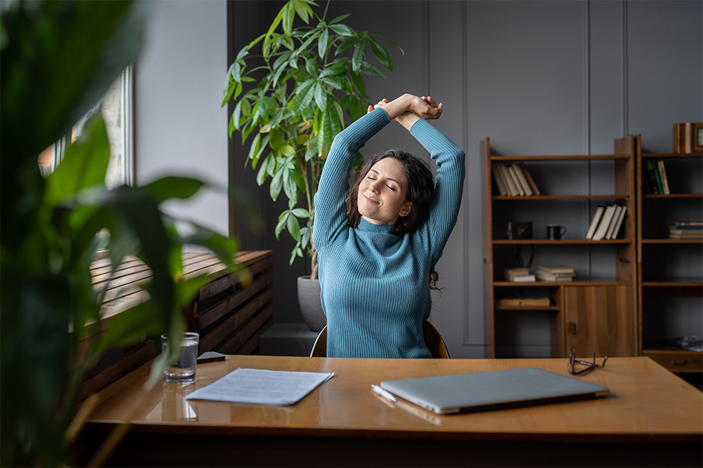 Woman at desk in office happy stretching out arms smiling relaxed and satisfied.