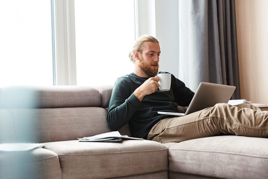 Concentrated young bearded man sitting in home using laptop computer