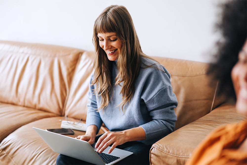 Happy business woman using a laptop in a light-filled room on a lounge.