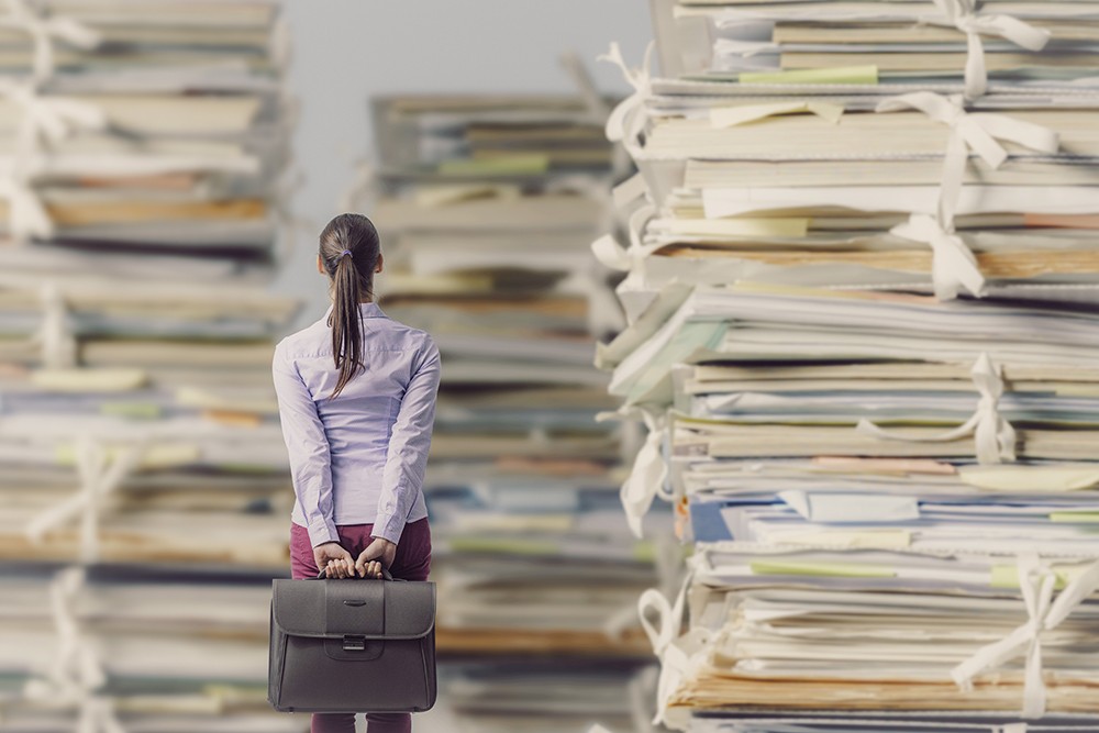Knowledge management concept. Picture of woman standing in front of piles of paper.