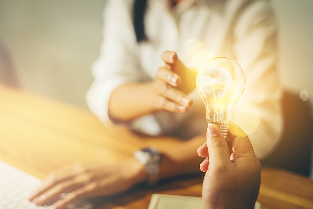 Office woman being handed a light globe. Sharing an idea concept.