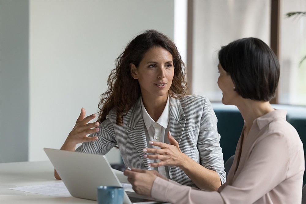 Business women sitting at desk discussing work collaborating.