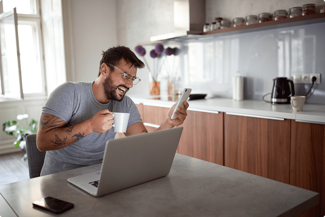 Happy businessman working from home with laptop and mobile phone and coffee laughing.